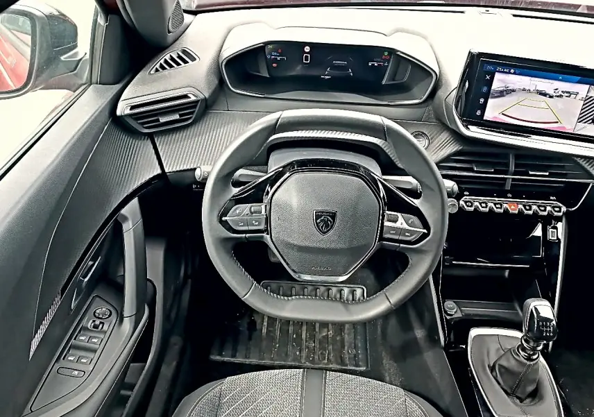 Vue intérieure centrée sur le volant Peugeot 2008 1.2 100 Allure avec tableau de bord digital et levier de vitesse manuel.