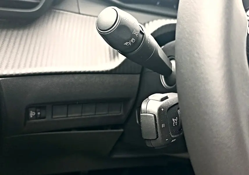 Gros plan sur la manette de commandes au volant côté gauche dans l'habitacle sombre du Peugeot 2008 rouge Elixir.