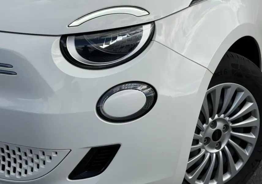 Gros plan sur l'avant droit blanc Artic du FIAT 500 électrique, mettant en valeur le phare rond et la jante alu 16 pouces.