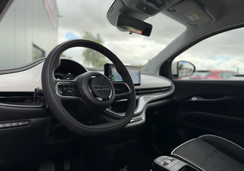 Vue intérieure côté conducteur de la Fiat 500 électrique 2024 avec tableau de bord blanc Artic et volant noir Soft-Touch.