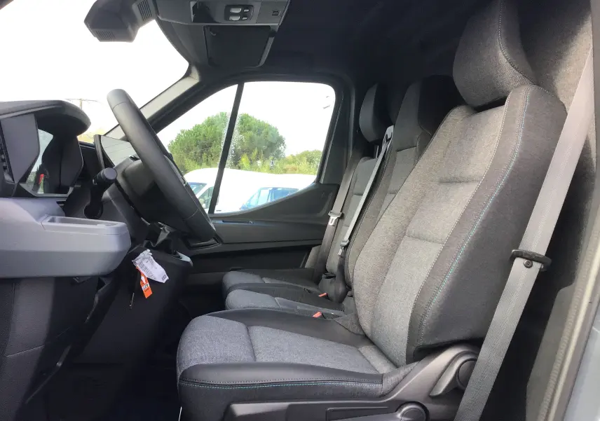 Vue intérieure côté conducteur du Renault Master 2025, montrant les sièges gris urbain avec surpiqûres bleues et le volant.