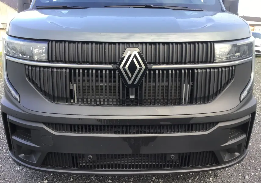 Vue frontale rapprochée du Renault Master gris urbain 2025 avec calandre noire et logo central proéminent.