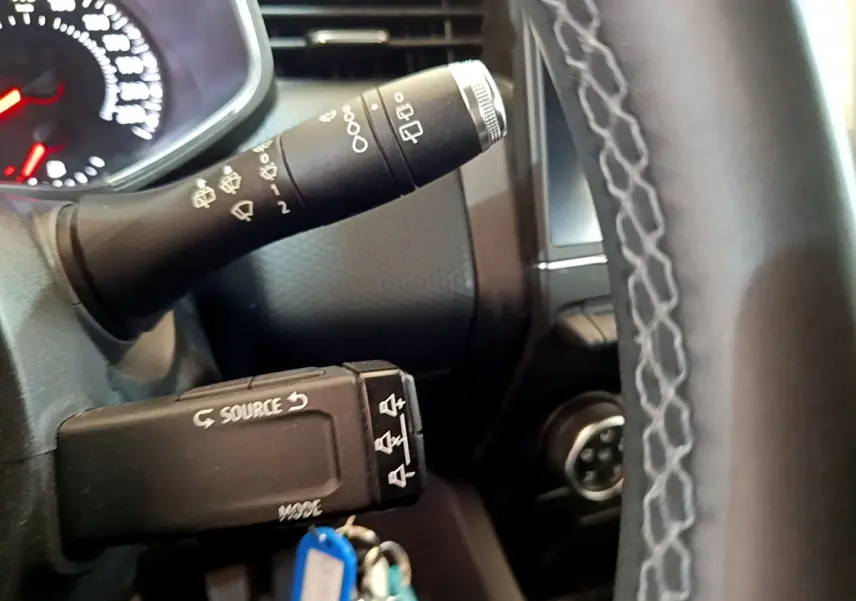 Gros plan sur la manette de commandes au volant et le volant en cuir synthétique de la Renault Clio blanche 2020.