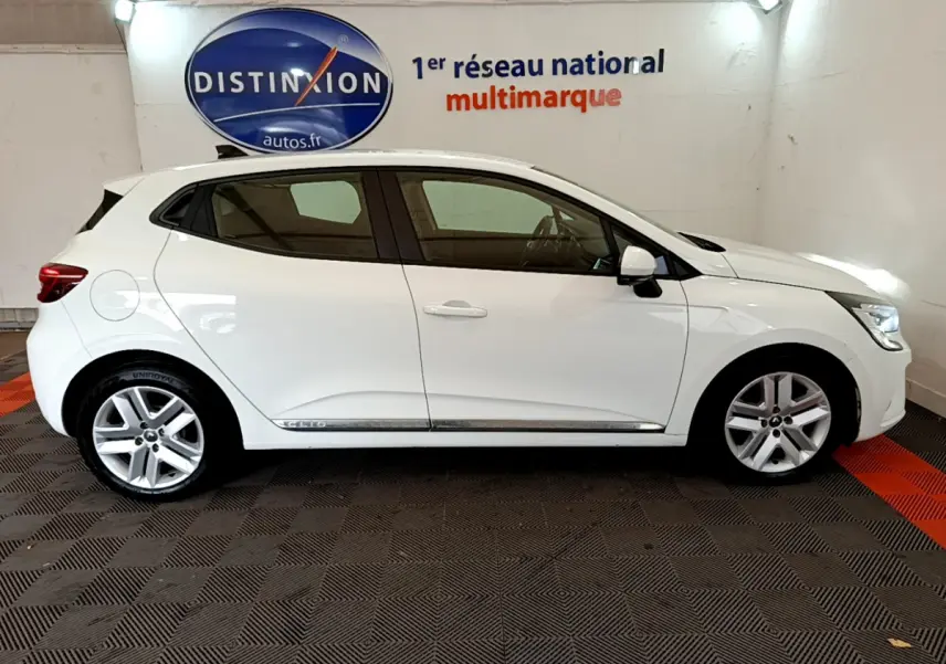 Profil droit d'une Renault Clio Business Blue dCi 85 blanche, avec jantes alliage et rétroviseurs blancs dans un showroom.