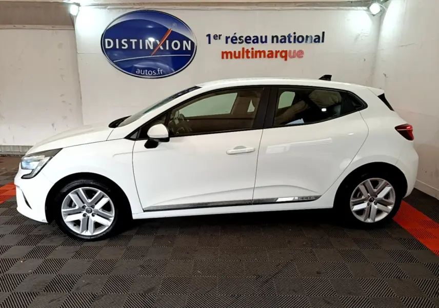 Profil droit d’une Renault Clio Business Blue dCi 85 blanche, avec jantes alliage et feux arrière LED visibles en intérieur showroom.