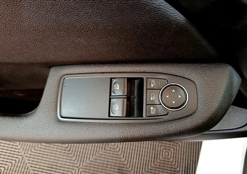 Gros plan sur les commandes de lève-vitres et rétroviseurs sur la porte côté conducteur d’une Renault Clio blanche.