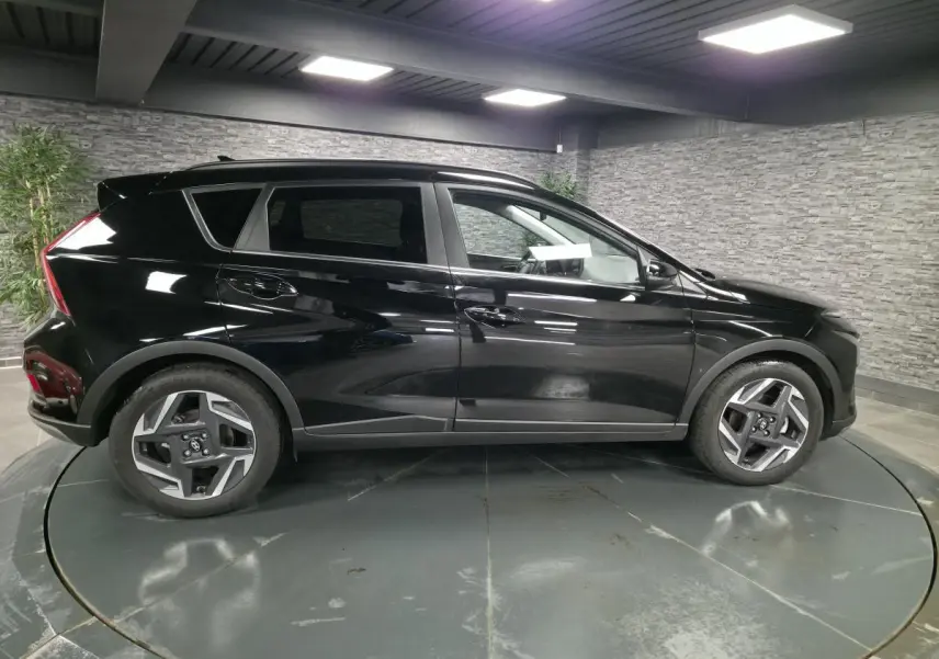 Profil côté gauche d'un Hyundai Bayon noir brillant, avec jantes alliage 17 pouces, dans un showroom intérieur.