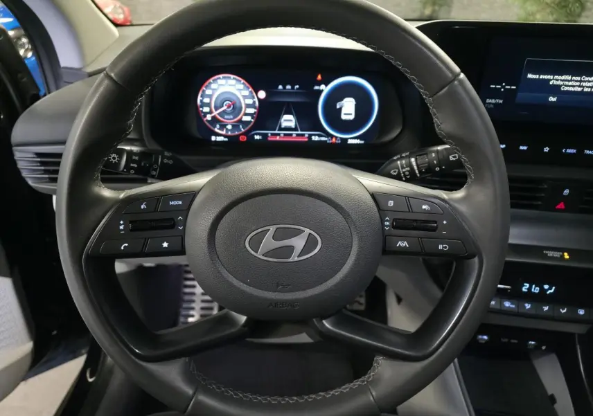 Vue intérieure centrée sur le volant cuir noir d'une Hyundai Bayon 2025 avec tableau de bord numérique et écran tactile.