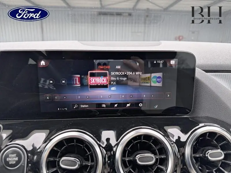 Vue intérieure centrée sur l'écran tactile multimédia et les aérateurs ronds d'une Mercedes Classe B noire cosmos métallisé.