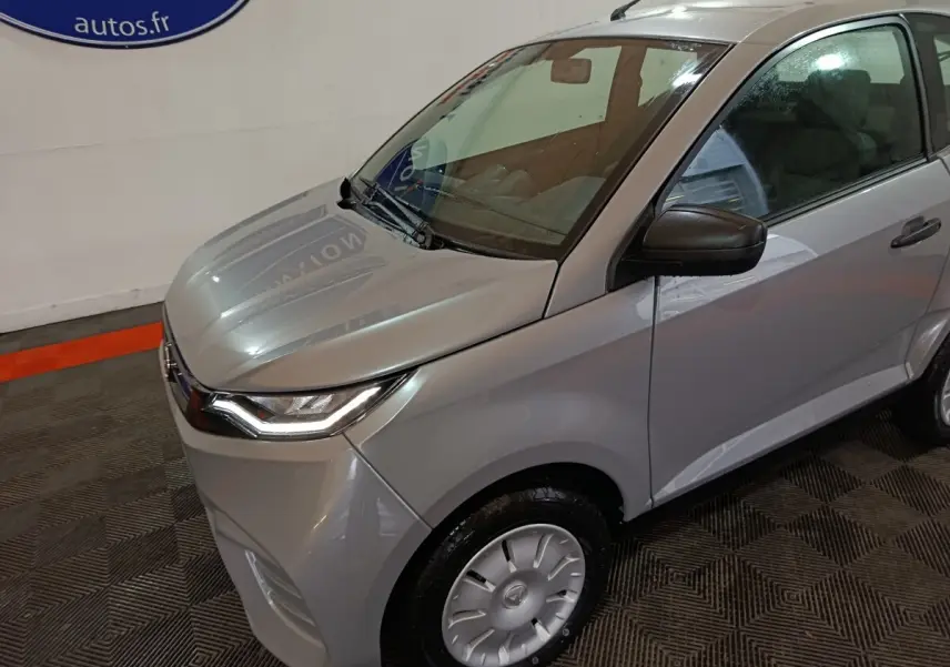 Vue 3/4 avant droit d'une Aixam Ambition 0.5 City Pack gris clair avec rétroviseur caméra côté conducteur.