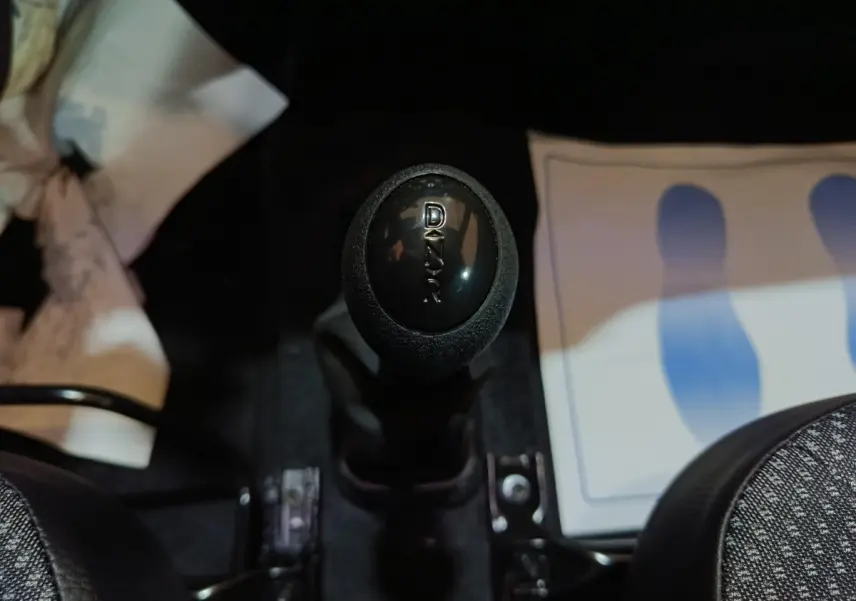 Le levier de vitesse noir marqué "DAKAR" au centre de l'habitacle d'une Aixam Ambition gris clair.