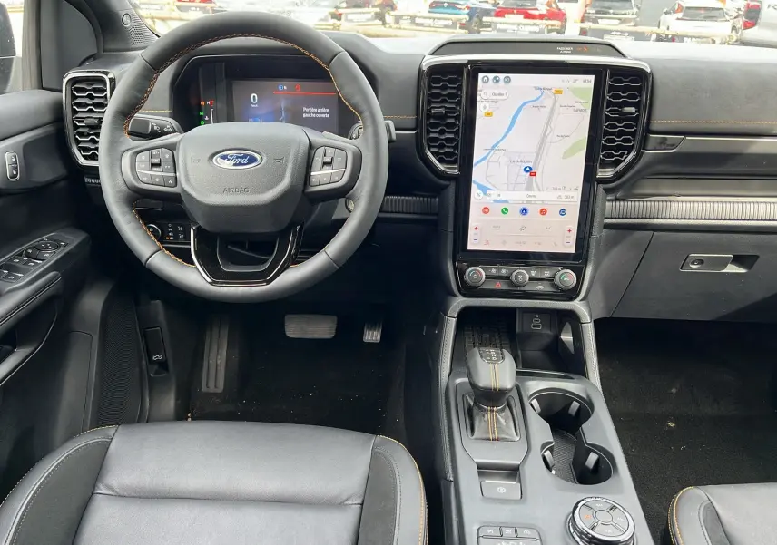 Vue intérieure avant du Ford Ranger gris carbone 2026, volant cuir multifonctions et grand écran tactile central avec GPS.
