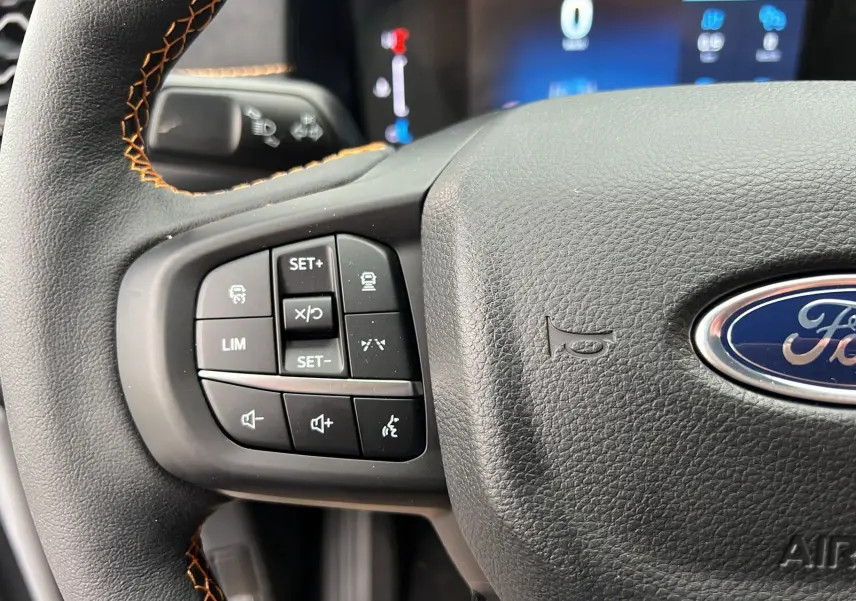 Gros plan sur le volant cuir noir du Ford Ranger gris carbone 2026, avec commandes multifonctions et surpiqûres orange visibles.