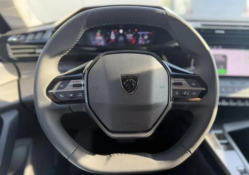 Vue rapprochée du volant cuir noir à méplat du Peugeot 308 2025 avec commandes intégrées et logo central.