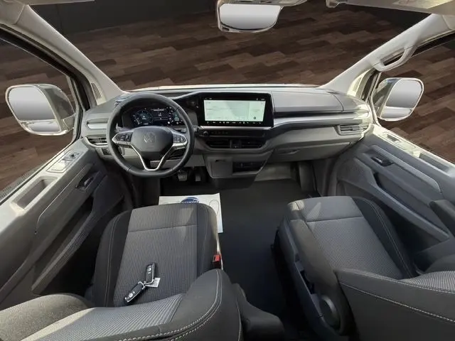 Vue intérieure avant du Volkswagen Transporter noir 2026, tableau de bord moderne avec écran tactile et volant multifonctions.