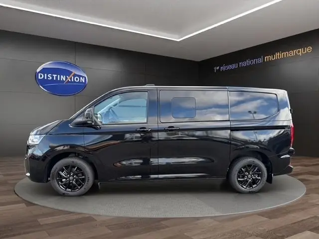 Vue de profil côté gauche d'un Volkswagen Transporter noir avec jantes noires, présenté en intérieur showroom.