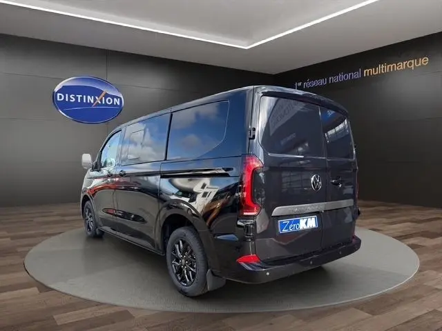 Vue 3/4 arrière droite d’un Volkswagen Transporter noir 2026, avec jantes noires et vitres teintées, en showroom.