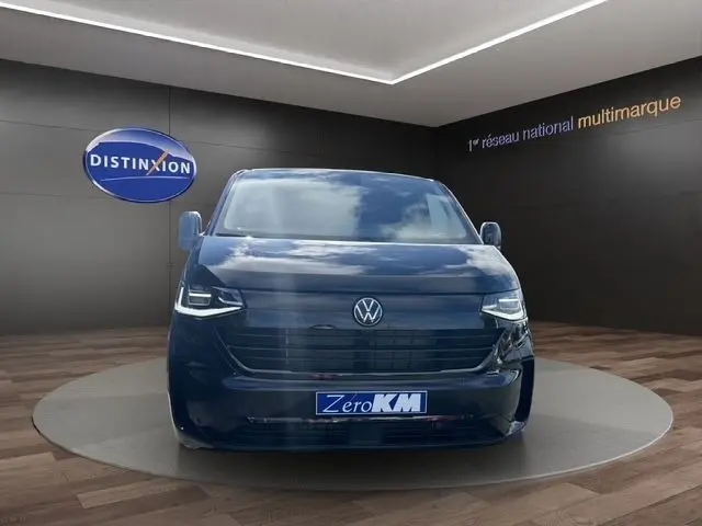 Vue frontale d'un Volkswagen Transporter noir 2026 avec phares LED et logo VW bien visible sur fond showroom.