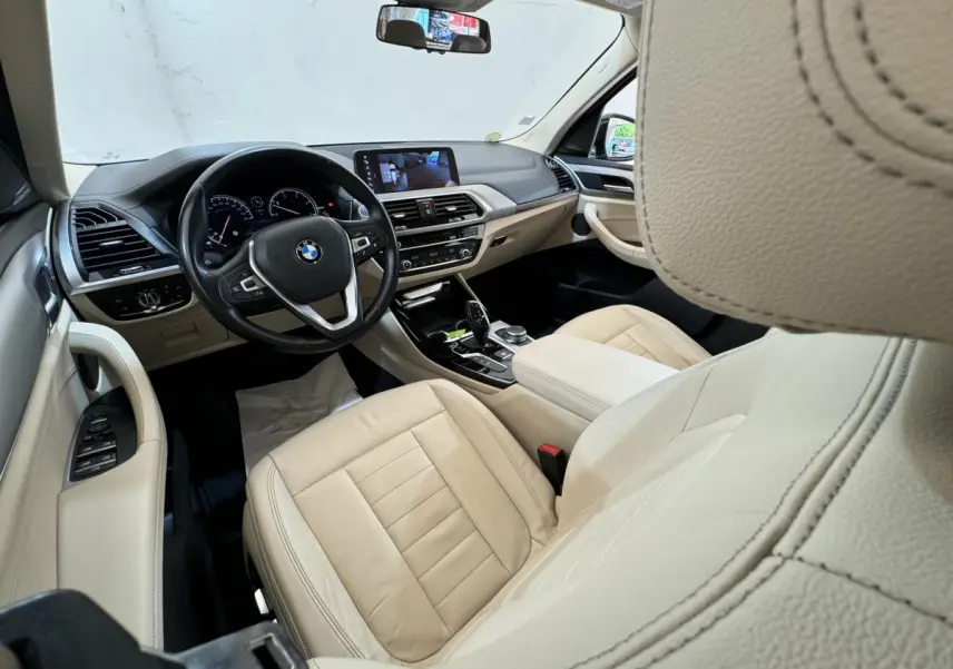 Vue intérieure côté conducteur du BMW X3 2018 avec sièges cuir beige et tableau de bord moderne avec écran tactile.