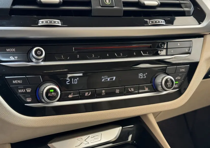 Détail du tableau de bord beige du BMW X3 xDrive30d 2018 avec commandes climatisation digitale et inscription X3.