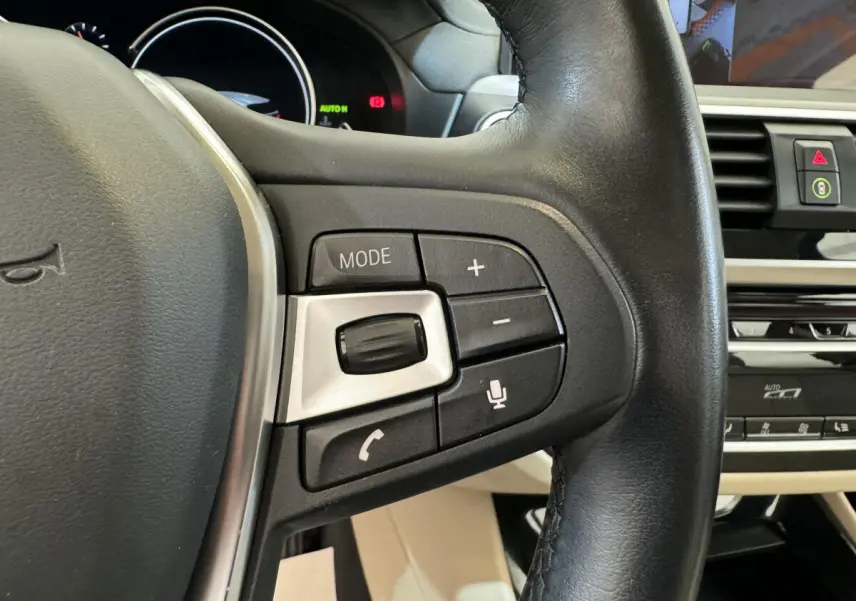 Gros plan sur le côté gauche du volant en cuir noir d'une BMW X3 gris foncé, avec commandes audio et vocales intégrées.