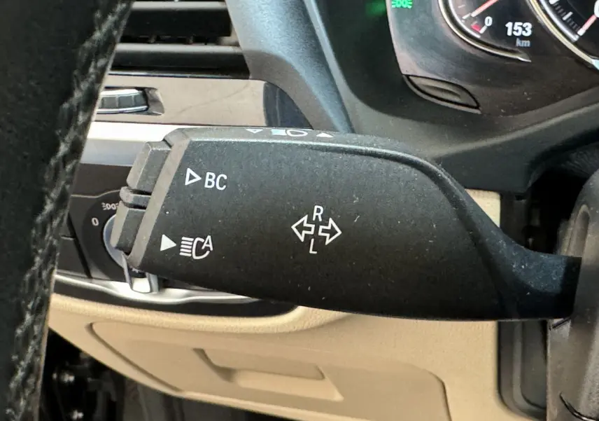 Gros plan sur la manette de clignotant noire à gauche du volant dans l'habitacle beige d'une BMW X3 gris foncé 2018.