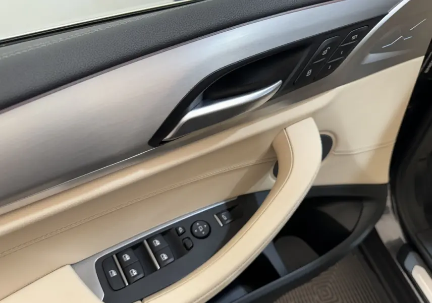 Détail de la porte avant gauche beige et aluminium brossé du BMW X3 xDrive30d 2018 avec commandes de vitres et mémoires de sièges.
