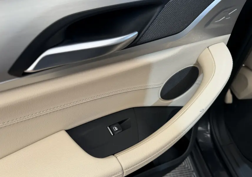 Poignée de porte intérieure beige côté conducteur du BMW X3 xDrive30d 2018 avec bouton de lève-vitre et haut-parleur intégré.