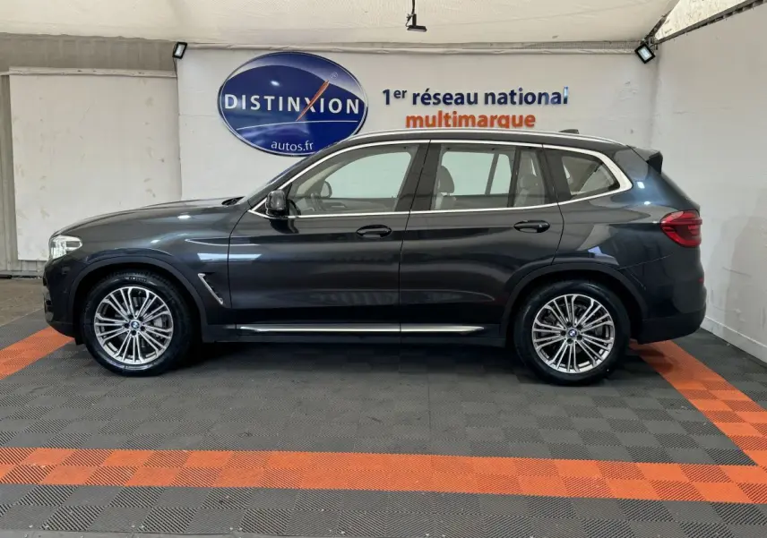 Profil droit d'un BMW X3 gris foncé 2018 Luxury avec jantes alliage et rails de toit chromés en intérieur showroom.