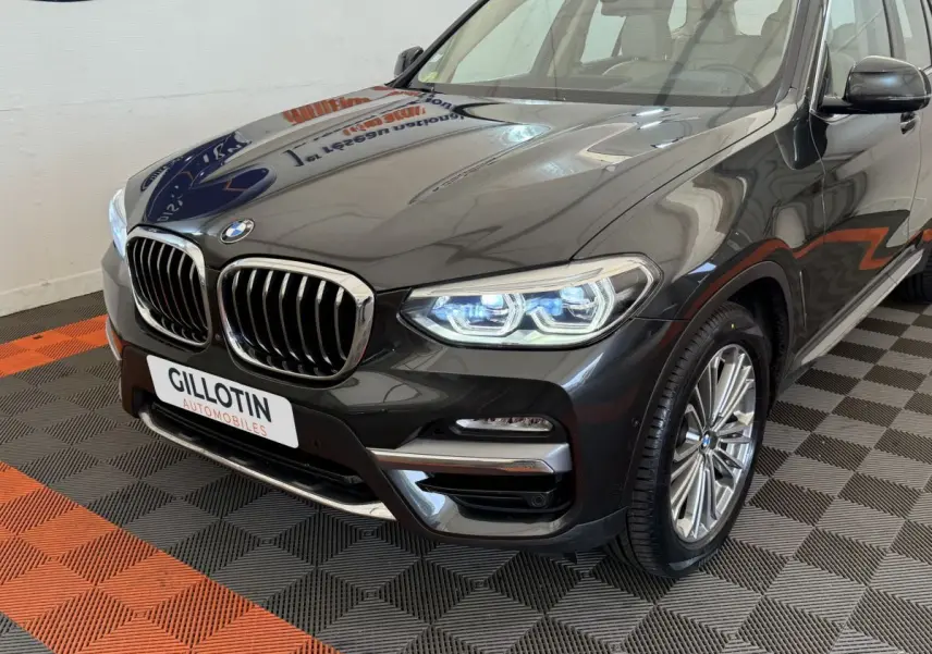 Vue 3/4 avant droit d’un BMW X3 gris foncé avec calandre chromée et phares LED allumés.