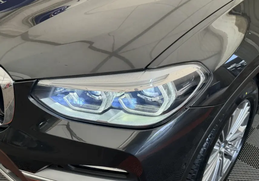 Gros plan sur le phare avant droit LED d'un BMW X3 gris foncé, avec jante alliage visible en arrière-plan.