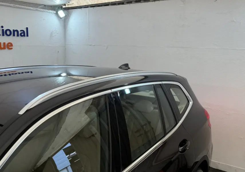 Vue latérale arrière droite d'un BMW X3 gris foncé avec barres de toit chromées dans un garage.