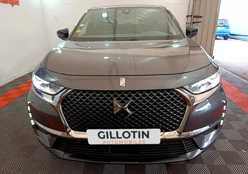 Vue frontale d'un DS7 Crossback gris foncé avec calandre noire à motif losange et phares LED allumés.