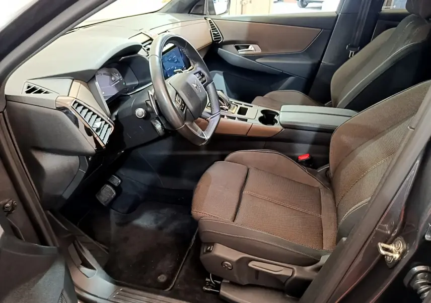 Vue intérieure côté conducteur du DS7 Crossback gris foncé, montrant le volant cuir, tableau de bord digital et sièges tissu foncé.