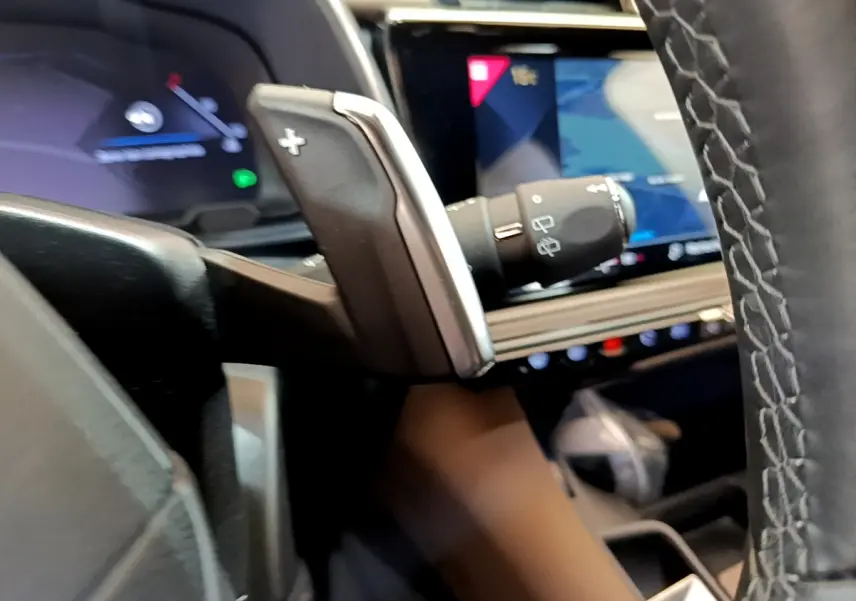 Gros plan sur la palette de changement de vitesse côté droit du volant cuir du DS7 Crossback gris foncé, avec écran tactile en arrière-plan.