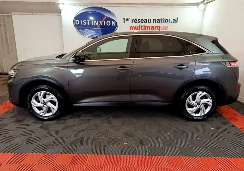 Vue de profil côté gauche d'un DS7 Crossback gris foncé garé en intérieur avec jantes alliage et vitres teintées.