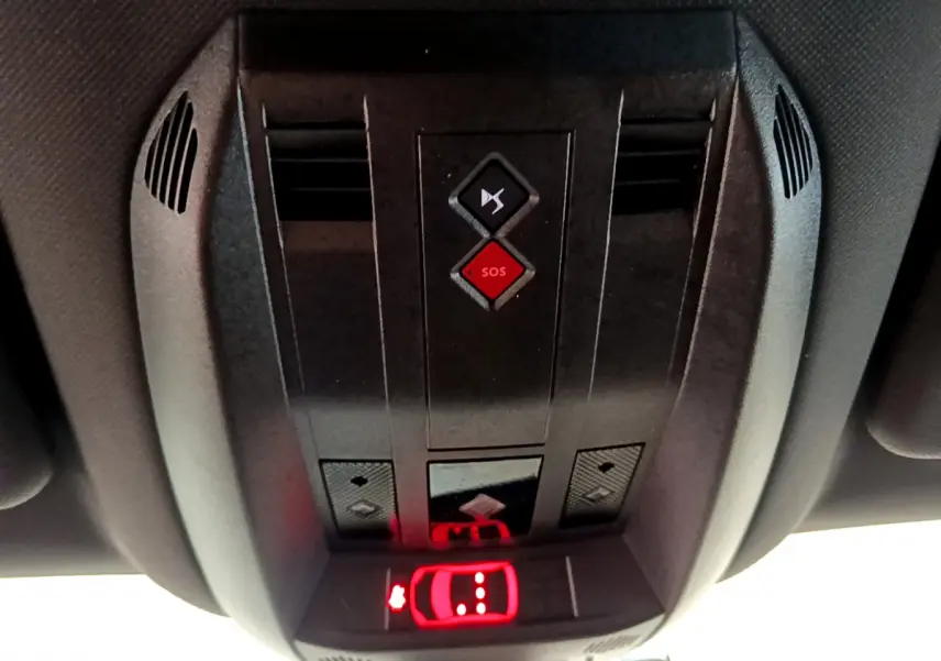 Vue en contre-plongée du panneau de commandes au plafond du DS7 Crossback gris foncé, avec bouton SOS rouge et éclairage rouge d'alerte.