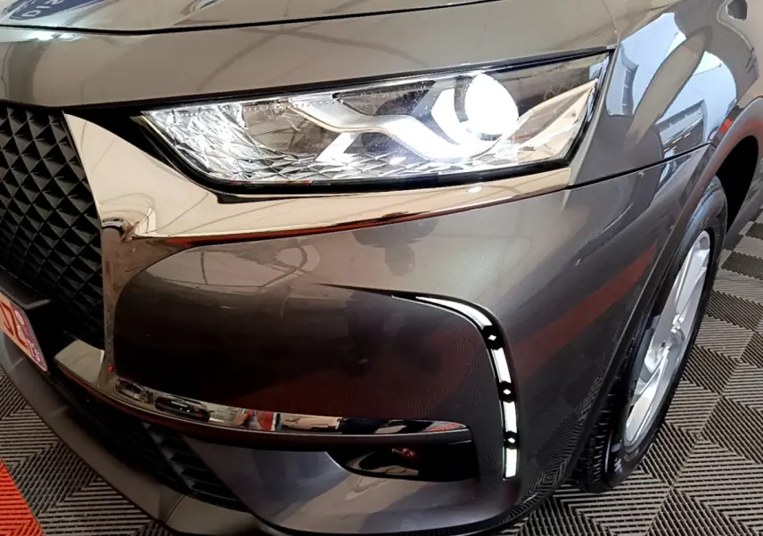 Gros plan sur le phare avant droit allumé du DS7 Crossback gris foncé, mettant en valeur la calandre et les feux LED distinctifs.