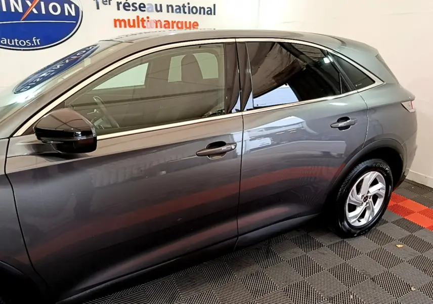 Vue latérale côté gauche d’un DS7 Crossback gris foncé garé en intérieur sur sol à motifs rouges et noirs.