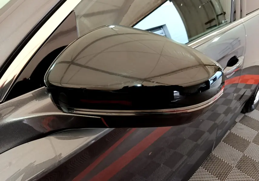 Rétroviseur droit noir brillant du DS7 Crossback gris foncé, vue rapprochée avec reflet de l'environnement intérieur.