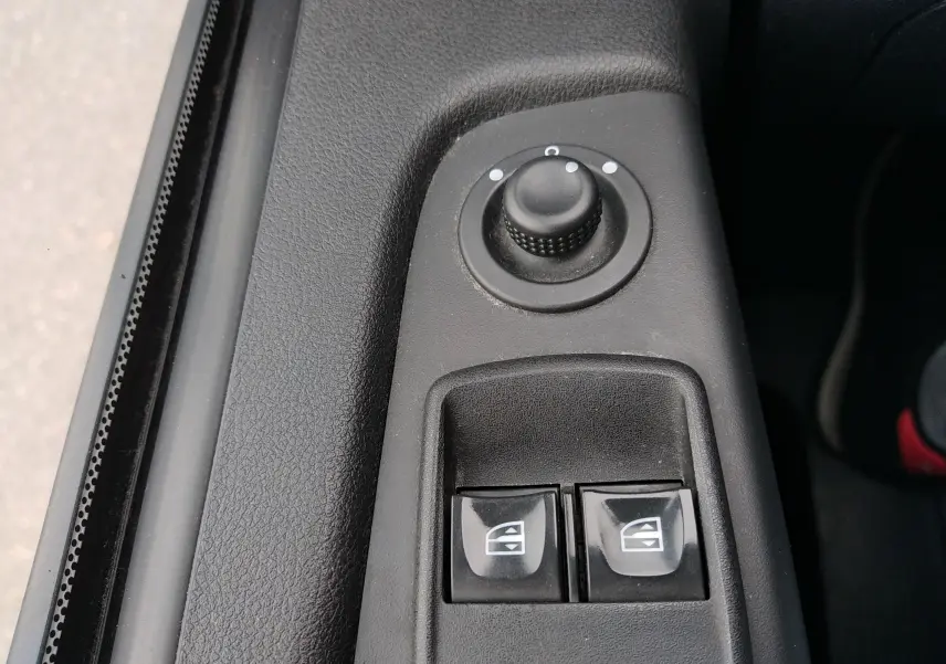 Gros plan sur les commandes de réglage des rétroviseurs et des vitres électriques côté conducteur d'un Renault Trafic Microbus blanc.