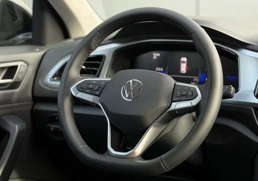 Vue rapprochée du volant cuir multifonction noir du Volkswagen T-Roc 2025 avec tableau de bord digital en arrière-plan.