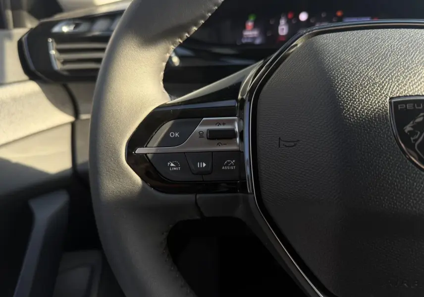 Gros plan sur le volant cuir noir de la Peugeot 308 2025, avec commandes intégrées et logo central visible.