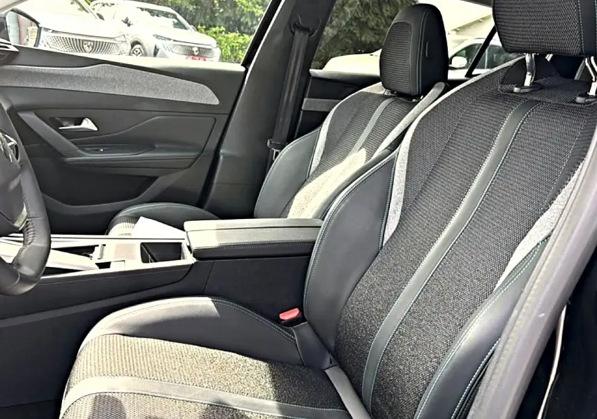 Vue intérieure côté gauche des sièges avant en tissu et cuir gris avec accoudoir central sur Peugeot 408 Hybrid 2024.