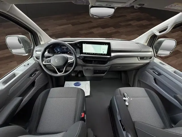Vue intérieure avant du Volkswagen Transporter gris foncé 2026, avec tableau de bord numérique et écran tactile central large.
