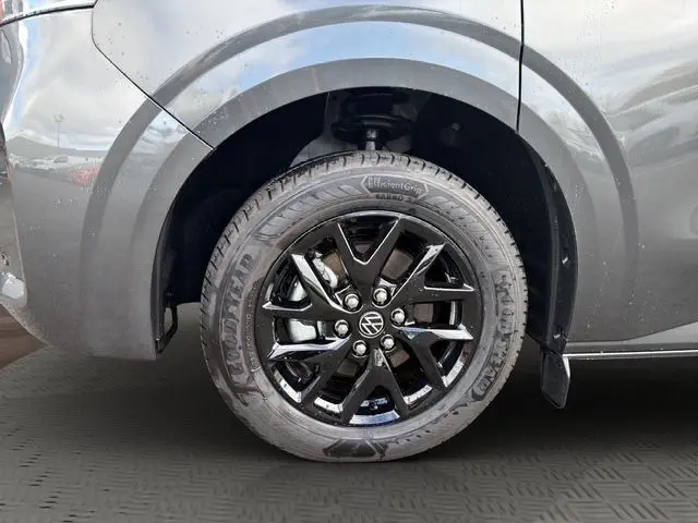Gros plan sur la roue avant droite noire brillante d’un Volkswagen Transporter gris foncé, avec logo VW central.