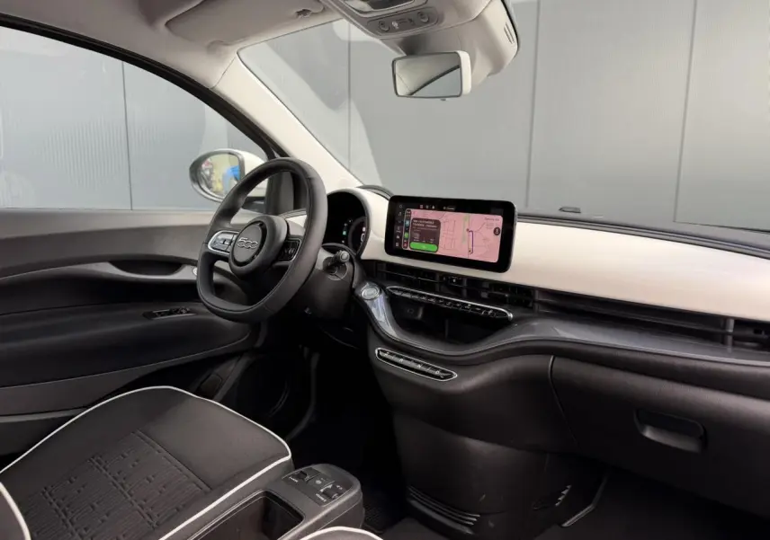 Vue intérieure côté conducteur du Fiat 500 électrique blanc Artic 2024, avec tableau de bord clair et écran tactile central.