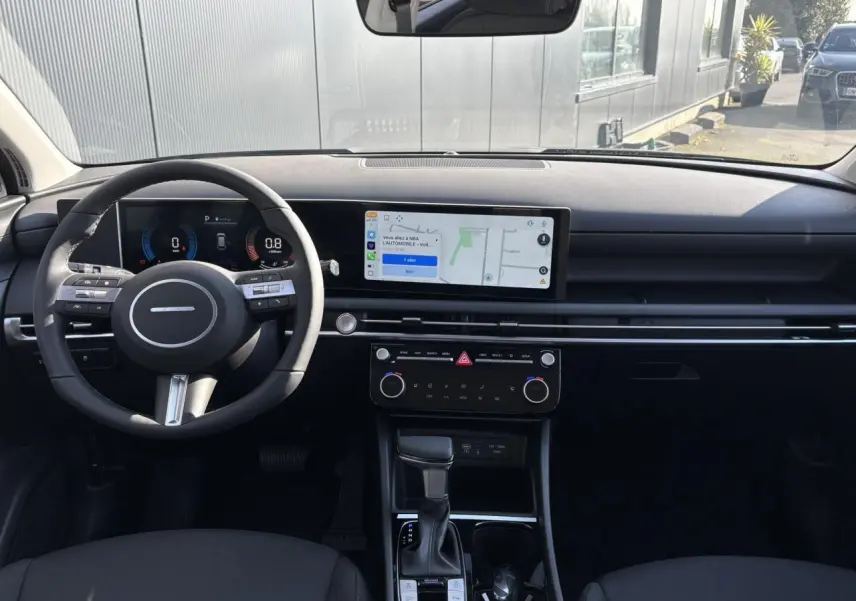 Vue intérieure frontale du tableau de bord du Hyundai Tucson 2025 avec écran tactile large et volant multifonction noir.
