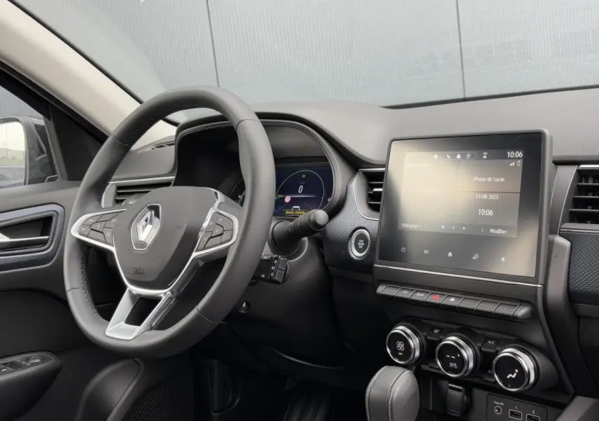Intérieur du Renault Arkana E-Tech 2024 vu côté conducteur, tableau de bord noir avec écran tactile central et volant multifonction.
