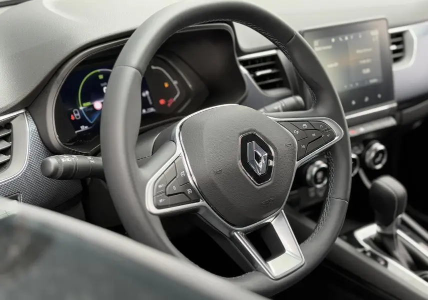 Volant Renault noir avec commandes intégrées, tableau de bord numérique et écran tactile au centre, vue intérieure avant.